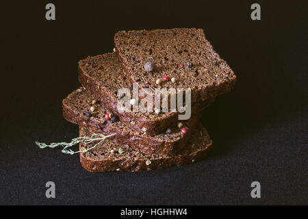 Vier Scheiben Brot mit Pfeffer-Mischung und einem Zweig Thymian auf dunklem Hintergrund Stockfoto