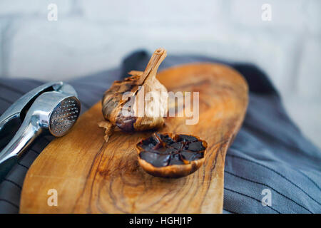 Schwarzer Knoblauch Zwiebeln und Knoblauchzehen auf hölzernen Hintergrund Stockfoto