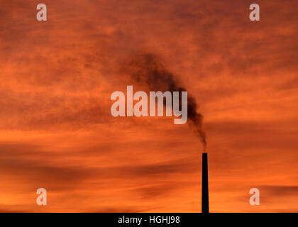 Rauch ausstoßen von einem Fabrikschornstein bei Sonnenuntergang. Stockfoto