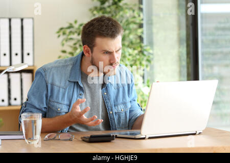 Wütend freiberufliche professionelle Probleme auf Linie mit einem Laptop in einem Desktop neben ein Fenster im Büro Stockfoto