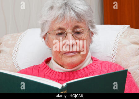 Ehemaliger senior Seniorin tragen Brille saß in einem Sessel entspannen und ein Buch zu Hause. England, UK, Großbritannien. Stockfoto