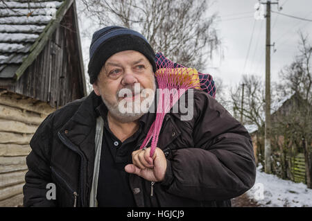 Outdoor Portrait positiv ukrainischen Bauern stehen auf einem ländlichen Dorf Straße und die Zeichenfolge-Tasche mit Haushalt Sachen Stockfoto