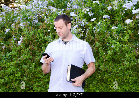 Lächelnder Mann sein Handy halten Sie eine Bibel zu betrachten. Stockfoto
