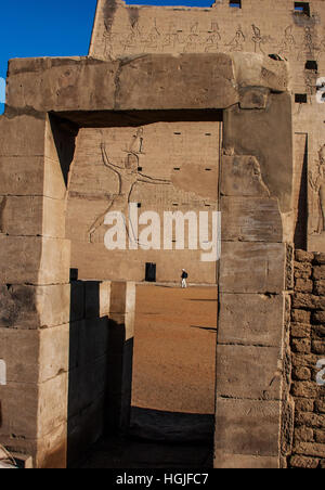 Mann, in den Schatten gestellt durch die Größe des Tempels von Edfu auf dem Nil in Ägypten, Köpfe, um einen kleinen Seiteneingang gesehen durch gerahmte Steinen Stockfoto