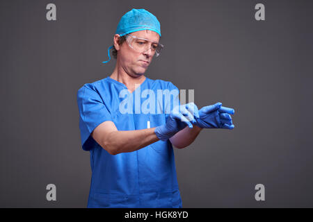 Ein mittleren Alters männlichen Arzt in blau scheuert nimmt seine Handschuhe und immer bereit Stockfoto