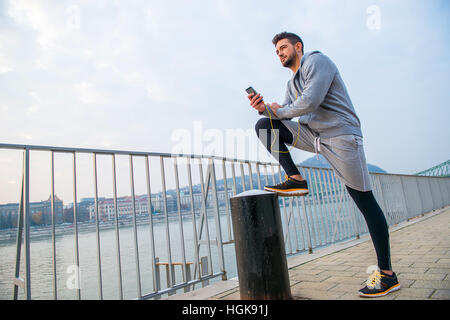 Ein hübscher junger Mann seinem Bein aufstellen und stützte sich auf es mit seinem Handy am Flussufer Stockfoto