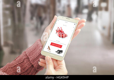 Frau mit Smartphone mit Commerce-Website. Freundliches app Benutzeroberfläche mit Frau Schuhe. Einkaufszentrum im Hintergrund. Stockfoto