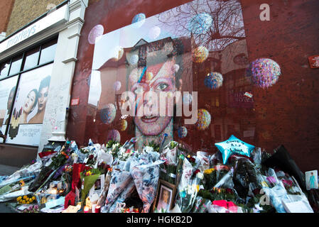 London, UK. 10. Januar 2017. Blumen und Ehrungen werden durch ein Kunstwerk von David Bowie auf einer Wand in Brixton, auf den ersten Todestag seines Todes, nur zwei Tage nach seinem 69. Geburtstag in London, UK gesetzt. Bildnachweis: Alberto Pezzali/Pacific Press/Alamy Live-Nachrichten Stockfoto