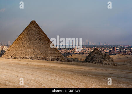 Die kleinste von den Pyramiden in Gizeh liegt in Trümmern, aber sein Nachbar ist noch intakt und die Stadt Kairo ist im Hintergrund Stockfoto