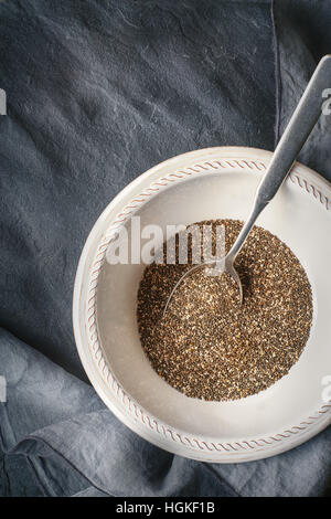 Chia-Samen in die weiße Platte mit Löffel auf dem dunklen Stein Tisch Stockfoto