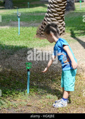 Kleiner Junge spielt mit Wasser aus einer Sprinkleranlage im Garten Stockfoto