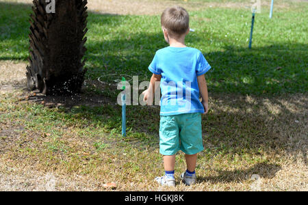 Kleiner Junge spielt mit Wasser aus einer Sprinkleranlage im Garten Stockfoto