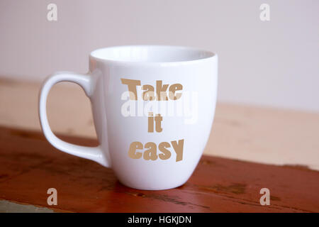 weiße Tasse mit den Worten Take It Easy auf roten Holztisch Stockfoto