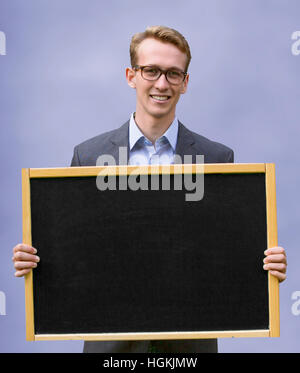 junger Mann im Anzug hält Tafel und lächelt Stockfoto