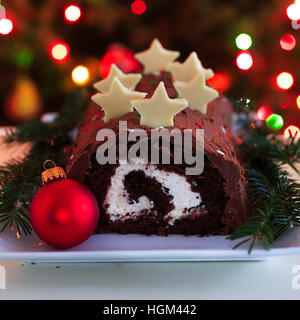 Hausgemachte Schokolade Yule Log Weihnachtskuchen vor dem Hintergrund der Weihnachtsbeleuchtung. Stockfoto