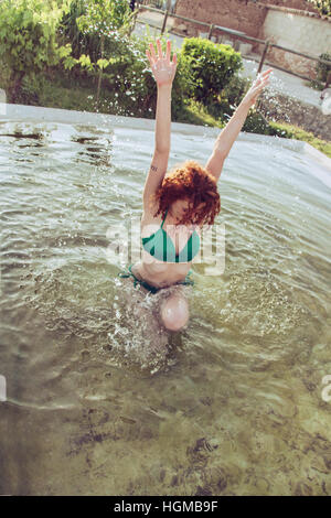 Junge Frau trägt einen grünen Bikini spielen mit Wasser in einem natürlichen Pool im Sommer Stockfoto