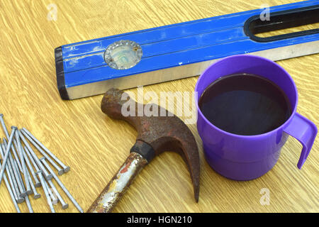 Kaffee-Haferl, alten Hammer, Nägel und Wasserwaage auf dem Tisch. Stockfoto