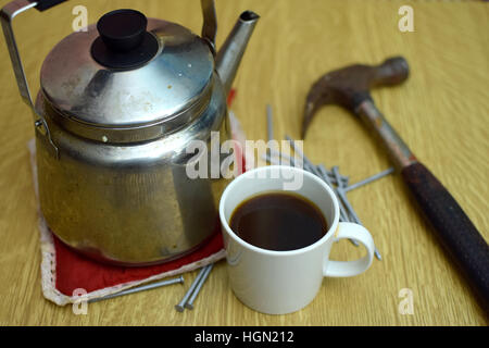 Kaffee-Pause. Kaffeekanne, Tasse, alte Hammer und Nägel auf dem Tisch. Tasse im Mittelpunkt. Stockfoto