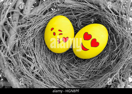 Zwei Ostereier bemalt mit Emojis, eins in der Liebe und anderen küssen, in ein Nest gelegt. Stockfoto