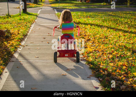 Ein junges Mädchen reitet ein Dreirad in einer kleinen Stadt in den Vereinigten Staaten. Stockfoto