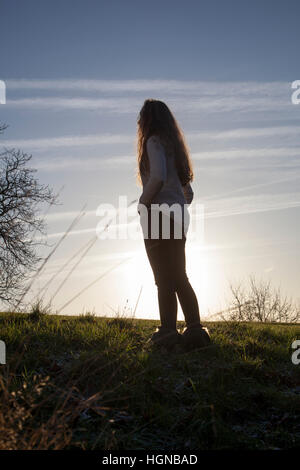 Junge Frau mit langen dunklen Haaren stehen wieder zur Kamera, Blick auf den Sonnenuntergang. Stockfoto