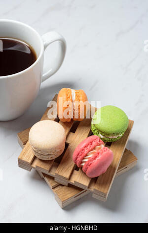 Süße und bunte Makronen auf wenig Holzpaletten mit Tasse Kaffee auf einem Marmor Textur Hintergrund serviert. Traditionelles französisches Dessert. Textfreiraum Stockfoto