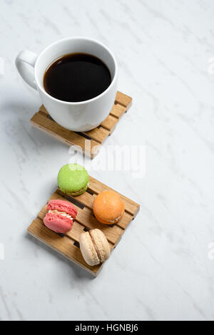Süße und bunte Makronen auf wenig Holzpaletten mit Tasse Kaffee auf einem Marmor Textur Hintergrund serviert. Traditionelles französisches Dessert. Stockfoto