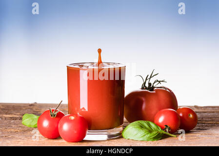 Tomatensaft spritzt über das Glas auf dem Holztisch Stockfoto