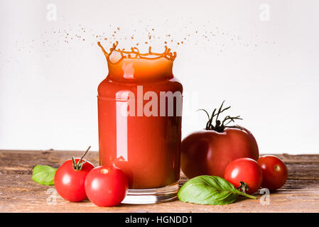 Tomatensaft spritzt über das Glas auf dem Holztisch Stockfoto