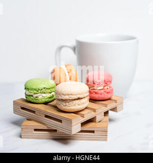 Süße und bunte Makronen auf wenig Holzpaletten mit Tasse Kaffee auf einem Marmor Textur Hintergrund serviert. Traditionelles französisches Dessert. Stockfoto