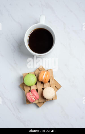 Süße und bunte Makronen auf wenig Holzpaletten mit Tasse Kaffee auf einem Marmor Textur Hintergrund serviert. Traditionelles französisches Dessert. Ansicht von oben. Stockfoto