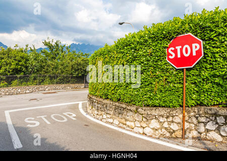 Kreuzung mit Stopp-Symbol gemalt auf Asphalt und roten sechseckigen Stoppschild auf Metallstab. Ländliche Straße in der Nähe der Stadt Como, Italien Stockfoto