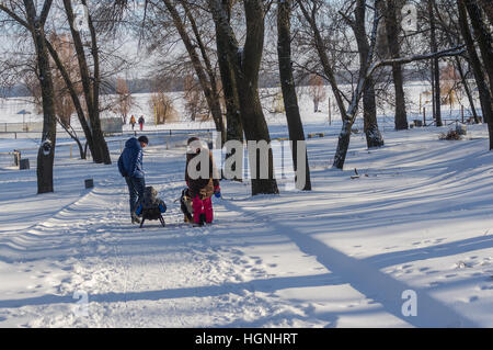 DNEPR, UKRAINE - 08 Januar 2017:Man mit Kind auf einem Schlitten vorbei an Frau mit großer Hund (Berner Sennenhund) Wandern im verschneiten Winter Park in Dnepr Stadt Stockfoto