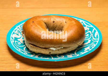 Bagel mit Frischkäse auf blauem Papierteller auf Holztisch Stockfoto