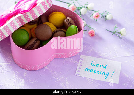 Becher Kuchen Macaron, Blatt Notebook Inschrift guten Morgen auf lila Tischplatte. Das gemütliche Frühstück. Kopieren Sie Raum. Stockfoto