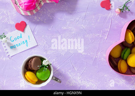 Frühstück, Muttertag, Geburtstag Hintergrund. Becher Kuchen Macaron, Blatt Notebook Inschrift guten Morgen auf lila Tischplatte. Kopieren Sie Raum. Stockfoto