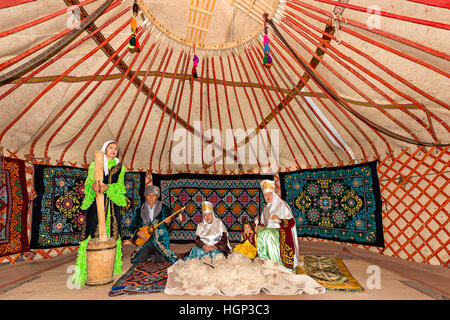 Kasachen in einer nomadischen Jurte mit einer Frau, die spinnt die Wolle und ein Mann spielen lokale Musikinstrument der Dombura in Almaty, Stockfoto