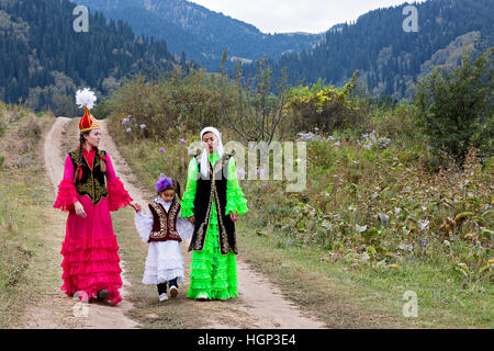 Kasachische Frauen in Nationalkostümen und ein Mädchen, das in der Natur in Almaty, Kasachstan, spazierengeht Stockfoto