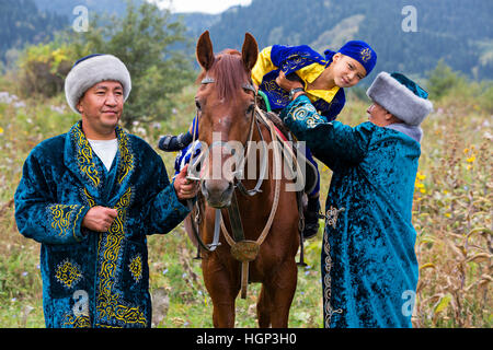 Kasachische Mann in Trachten hilft den jungen von seinem Pferd in Almaty, Kasachstan Stockfoto