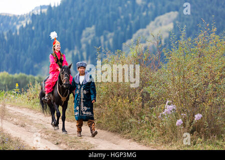 Kasachische Paar in Volkstrachten mit einer einheimischen Frau auf dem Pferd, Kasachstan Stockfoto