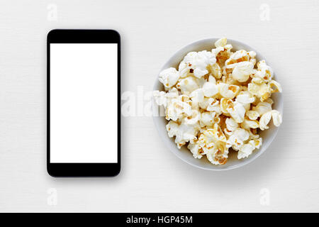 Smartphone und Popcorn in Schüssel auf weißen Tisch Stockfoto