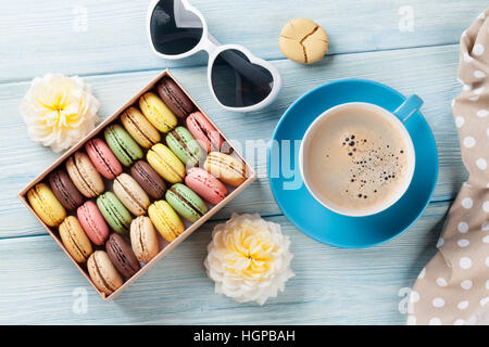 Bunte Makronen und Kaffee auf Holztisch. Süße macarons in Geschenkbox und Blumen. Ansicht von oben Stockfoto