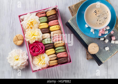 Bunte Makronen und Kaffee auf Holztisch. Süße macarons in Geschenkbox und Blumen. Ansicht von oben Stockfoto