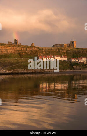 Blick auf die East Cliff (Häuser, Kirche St. Marien, Abtei Ruinen und Regenbogen) spiegelt sich in den Meer - Whitby, North Yorkshire, GB. Stockfoto