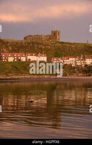 Schlauchboot Whitby Hafen kreuzt, East Cliff und St. Marien Kirche hinaus spiegelt sich in den Meer - North Yorkshire, GB. Stockfoto