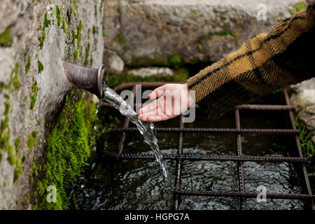 Kleine Hand eines Mädchens berühren Wasser aus einem natürlichen Brunnen Stockfoto