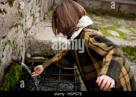 Kleine Mädchen berühren Wasser aus einem natürlichen Brunnen Stockfoto