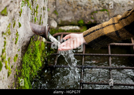 Kleine Hand eines Mädchens berühren Wasser aus einem natürlichen Brunnen Stockfoto