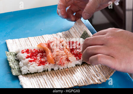 Nahaufnahme der Köche Hände verdrehen sich Matte mit Zutaten zu Futomaki Sushi-Rollen Stockfoto