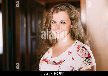 Das Porträt der jungen schönen Plus Size kaukasischen glücklich lächelnde Mädchen Frau mit blauen Augen und wellige braune lange Haare zu Hause Stockfoto